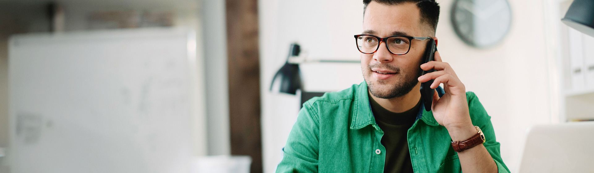 Mann mit Brille telefoniert am Schreibtisch im Büro