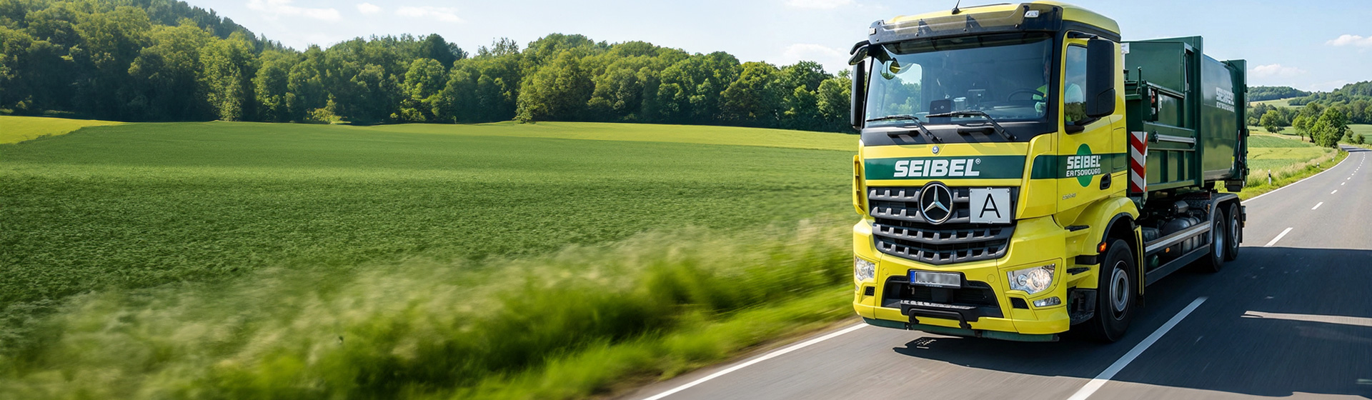 Gelber Seibel-Entsorgungs-Lkw fährt auf Landstraße durch grüne Landschaft